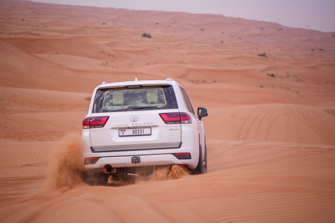 A Toyota Land Cruiser drives actively through a vast desert, showcasing offroad capabilities.