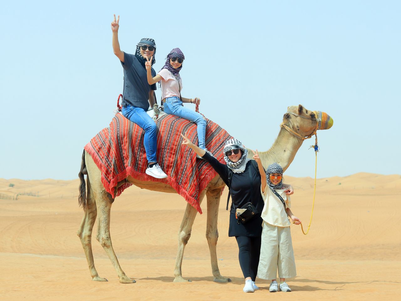 A joyful family posing with a camel in the Dubai desert, capturing the essence of adventure.