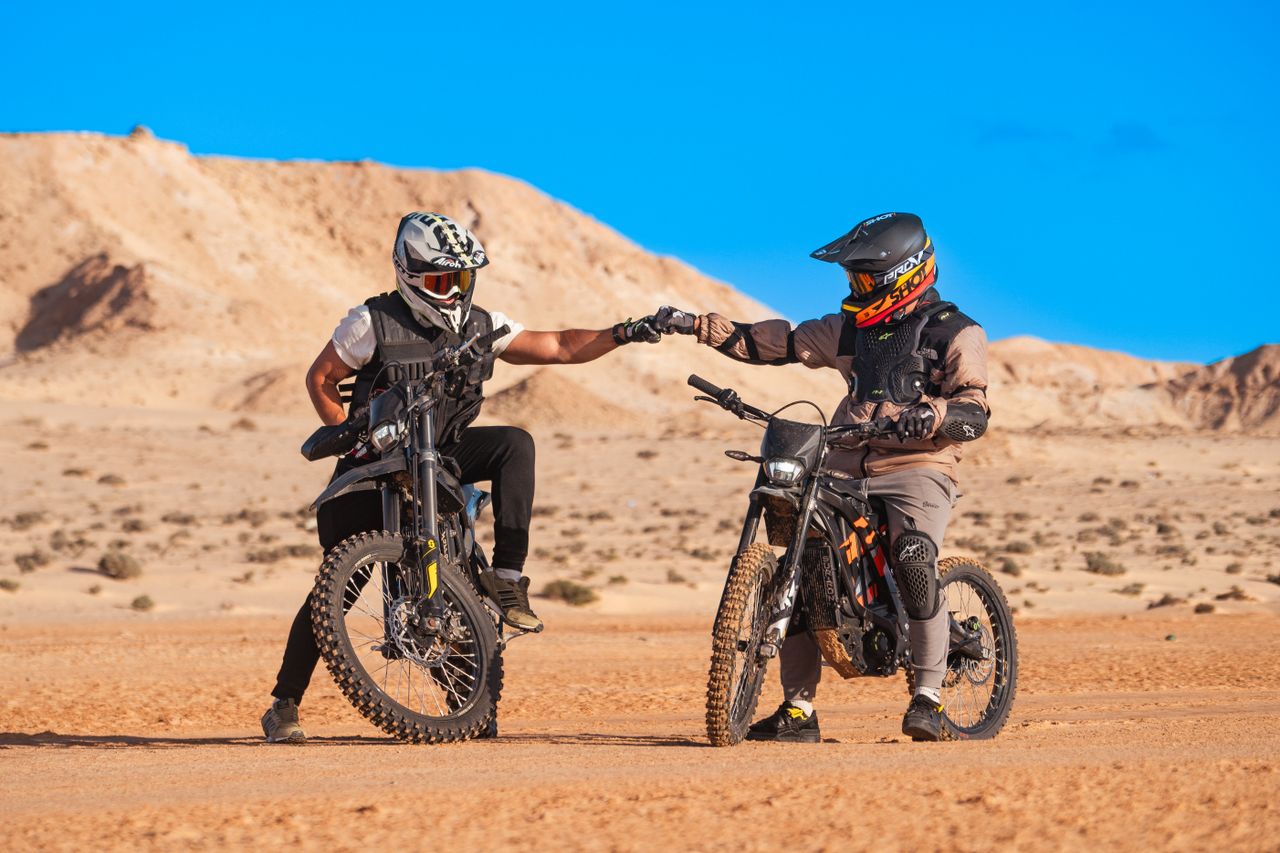 Two motocross riders celebrate a fist bump in the striking desert landscape of Dakhla.
